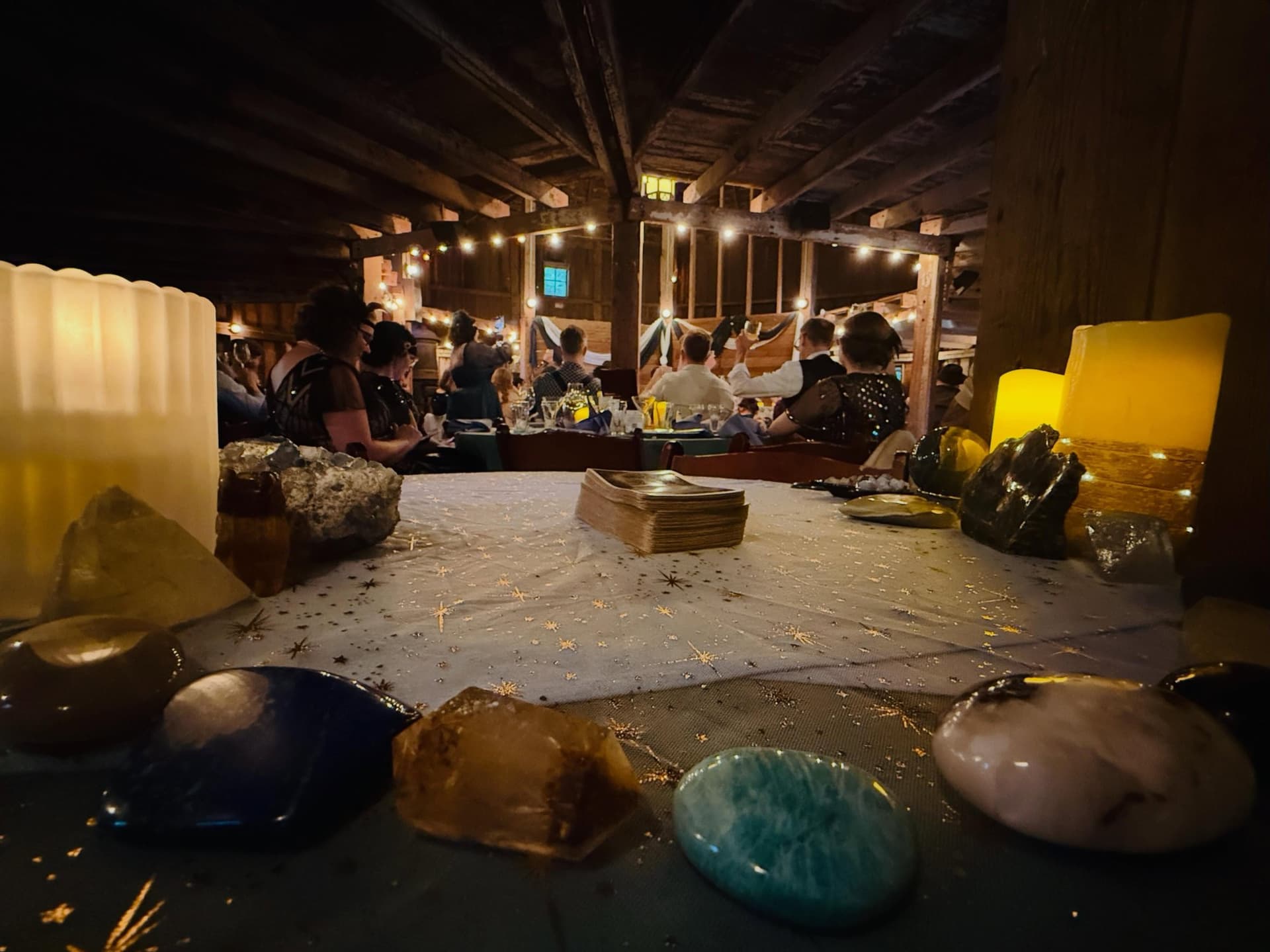 Holly's candlelit tarot table set with crystals and a deck at a 1920s-themed wedding in a barn full of guests